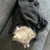 Perro pequeño de pelo claro cubierto parcialmente con manta de tela gris oscuro sobre sofá gris. Se muestra la textura de la manta y el tamaño relativo respecto al perro.