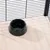 Black plastic food bowl on light wooden floor, surrounded by metal mesh walls.
