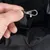Close-up of a metal carabiner on a black strap, held by a hand.