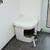 Katzentoilette mit weissem Gehäuse und seitlichem Eingang. Katze verlässt die Toilette. Geeignet für diskrete Platzierung in Wohnräumen.