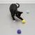 Chat noir et blanc jouant avec trois balles texturées de couleurs jaune, violette et bleue sur un sol gris. Les balles semblent en tissu ou matière souple.