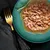 Chunks of wet food in gravy served on a green plate with a sprig of rosemary, shown for product texture and appearance.