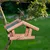 Casita para pájaros colgante de madera con techo verde, llena de alimento para aves, fijada a una rama en el jardín.
