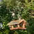 Casita para pájaros colgante de madera con techo verde, fijada a una rama. Adecuada para alimentar aves silvestres en el jardín.