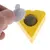 Gelbes dreieckiges Spielzeug mit herausnehmbarem Deckel, darunter ein grüner Ball aus gepresstem Material. Hand zeigt Öffnung des Deckels.