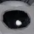 Grey pet bed with cave entrance and hanging white plush ball. Interior made of black fabric, top lying surface made of soft grey material.
