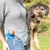 Person hält einen Hund und trägt einen blauen Ballwerfer mit orangefarbenem Ball in der Hosentasche.