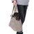 Petit chien noir et marron dans un sac de transport en tissu beige porté à la main par une personne en pull gris et pantalon foncé. Sac avec anses épaisses, matière effet polaire.