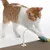 Rote und weisse Katze spielt mit einem Spielzeug auf einer Kratzmatte. Das Spielzeug ist an einer Metallfeder befestigt.