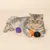 Gatto grigio con tre palline da gioco colorate in viola, arancione e nero su sfondo beige.