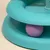Jouet pour chat en plastique turquoise avec une balle violette visible à l'intérieur d'une piste circulaire.