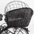 Panier en osier noir avec grille métallique, fixé à l’arrière d’un vélo, coussin gris visible au fond du panier.