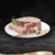 Куски мясного паштета на белой тарелке с золотистой вилкой и веточкой зелени, черный фон. Вид продукта без упаковки.
