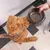 Hund nimmt Futter aus einem schwarzen Napf mit Marmormuster, der von einer Hand gehalten wird. Einige Kroketten sind im Napf sichtbar.