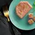 Pâtée pour animaux en tranche et en cubes, morceaux visibles de légumes verts et orange, présentée sur une assiette turquoise avec une fourchette dorée à côté.