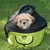 Sac de transport pour animal en tissu vert et noir, fermeture zippée partiellement ouverte, poignée sur le dessus, poche frontale visible, posé sur l’herbe.