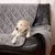 Graue gesteppte Sofadecke aus Stoff, drapiert über ein Ledersofa. Ein kleiner Hund liegt entspannt auf der Decke.