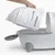 En hånd løfter låget af en hvid kattetoilet med aftagelig overdel og sideklap, indersiden med synlig strøelse.