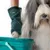 Hand mit grünem Reinigungshandschuh der Marke kooa reinigt die Pfote eines Hundes über einem Eimer.