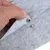 Detailaufnahme eines grauen Filzmaterials mit Druckknopfverschluss, gezeigt durch eine Hand, die den Stoff anhebt.