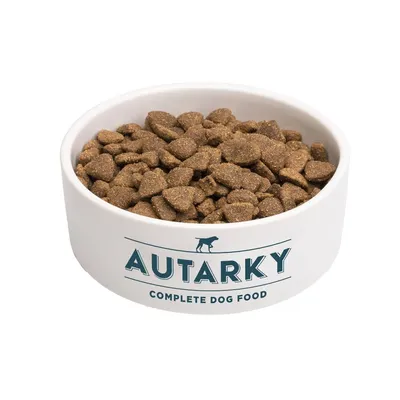 Bowl filled with brown kibble pieces. The bowl displays the text 'Autarky Complete Dog Food'.