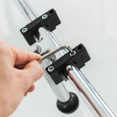 Mano che utilizza una chiave a brugola per fissare due tubi metallici con staffe nere e viti visibili.