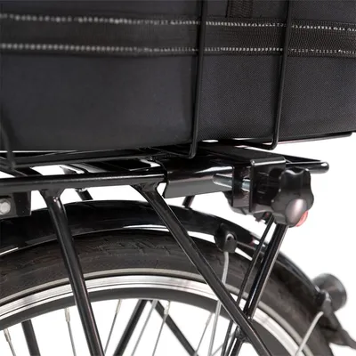 Dettaglio di portapacchi in metallo montato sulla ruota posteriore di una bicicletta, con fissaggio a vite e borsa nera sopra il portapacchi.