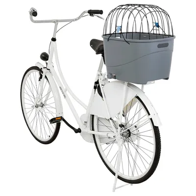 Vélo blanc avec panier de transport gris en plastique et grille métallique noire fixé sur le porte-bagages arrière, adapté pour transporter un animal ou des objets.