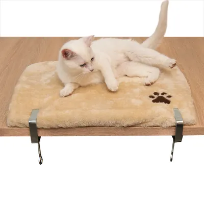 Beige kattenligbed van pluche met pootafdrukmotief, bevestigd op een houten plaat met metalen klemmen. Witte kat ligt er ontspannen op.