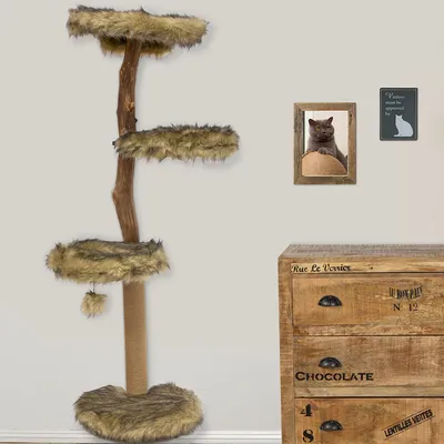 Tiragraffi per gatti con tre piattaforme rivestite in pelliccia sintetica, tronco centrale in legno e base rotonda, include una pallina appesa. Mobile in legno visibile a destra.