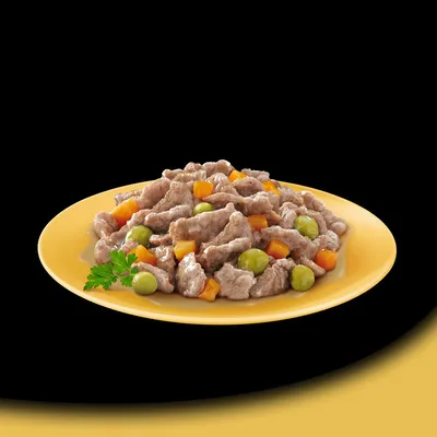 Keltainen lautanen, jossa lihapaloja kastikkeessa sekä vihreitä herneitä ja oransseja kuutioita, koristeena persiljan oksa.