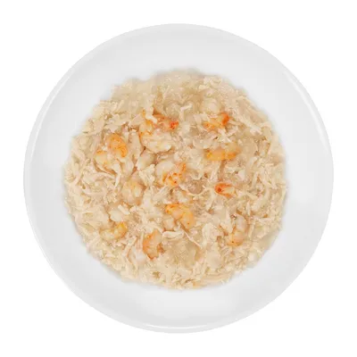 Natvoer op een wit bord met stukjes garnalen en geraspte witte ingrediënten, licht van kleur en vochtig van structuur. Geen merknaam of tekst zichtbaar.
