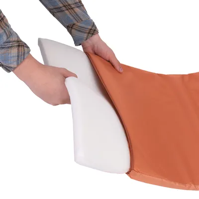 Kädet asettavat valkoista vaahtomuovityynyä oranssin kankaisen päällisen sisään. Materiaalit: vaahtomuovi ja kangas.