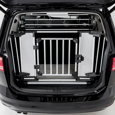 Transportbox aus Metall und Kunststoff im Kofferraum eines Autos, mit Gittertür und seitlichen Verstrebungen für sicheren Transport.