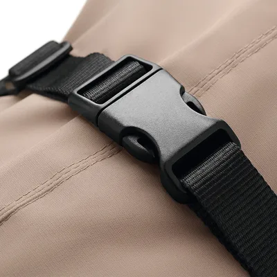 Zbliżenie na czarne plastikowe zapięcie z regulowanym nylonowym paskiem na beżowej tkaninie.