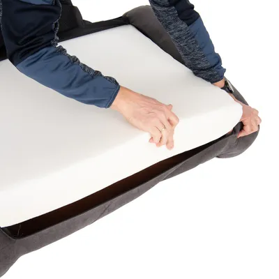 Persoon toont het plaatsen van een witte schuimrubberen matras in een grijze hoes, geschikt voor huisdierenbedden.