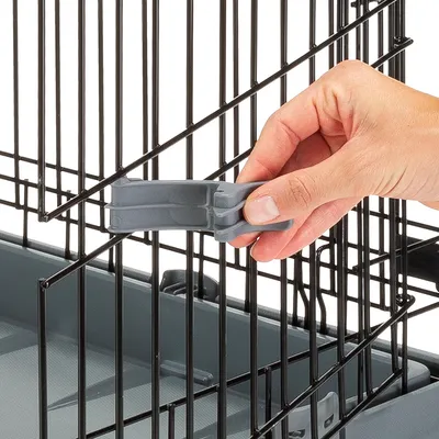 Hand zeigt, wie ein grauer Verschluss an einem Metallgitterkäfig geöffnet oder geschlossen wird.