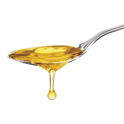 Metalen lepel met gele olie, een druppel olie valt van de lepel. Geen merknaam of tekst zichtbaar.