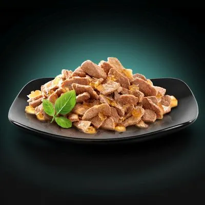 Stukjes natvoer in saus op een zwart bord, gegarneerd met een takje basilicum. Geen merknaam of verpakking zichtbaar.