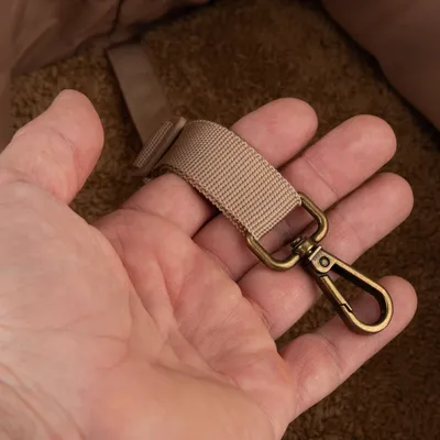 Beige nailonhihna metallisella karabiinihakalla, pidetään kädessä. Yksityiskohtainen kuva kiinnityselementistä.