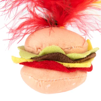 Jouet pour animal en forme de hamburger en tissu avec garnitures colorées et plumes rouges sur le dessus, aucun texte visible.