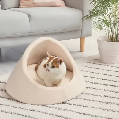 Cat cave made of beige fabric with soft padding, on a striped rug in a modern living room setting.