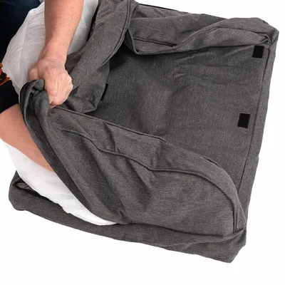 Hand plaatst wit kussen in grijze stoffen hoes met klittenbandsluitingen, detail van afneembare hondenbedhoes zichtbaar.