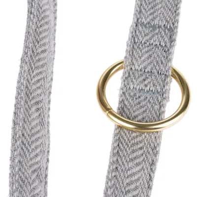 Detailaufnahme eines grauen Stoffbands mit Fischgrätenmuster und einem goldfarbenen Metallring.
