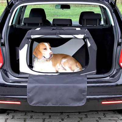 Hond ligt in opvouwbare transportbox van stof in de kofferbak van een auto, met open flap aan de achterzijde zichtbaar.