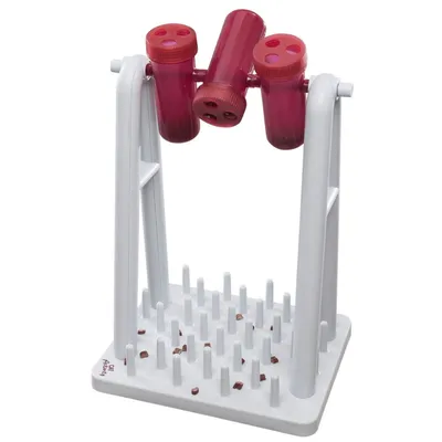 Gioco interattivo per animali in plastica con tre cilindri rossi forati su supporto bianco e base con pioli, alcuni bocconcini visibili sulla base.