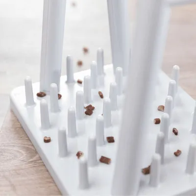 Gioco interattivo per animali in plastica bianca con pioli verticali e crocchette sparse sulla superficie.