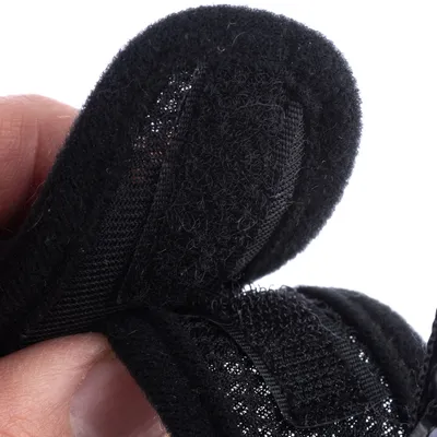 Detailný záber na čierny suchý zips s jemnou sieťovanou štruktúrou, drži ho ruka.