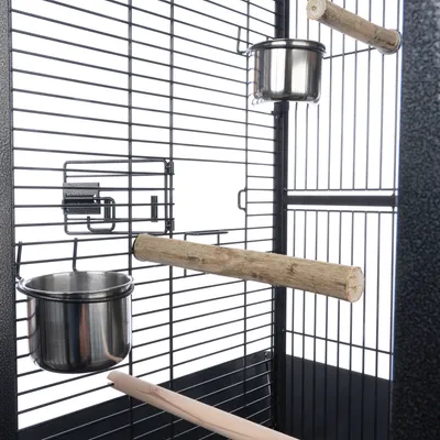 Intérieur de cage à oiseaux avec deux perchoirs en bois et deux gamelles en acier inoxydable fixées aux barreaux noirs.
