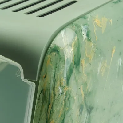 Detailní záběr na zelený plastový kryt s mramorovaným povrchem a zlatými akcenty. Viditelný recyklační symbol pro PP plast.
